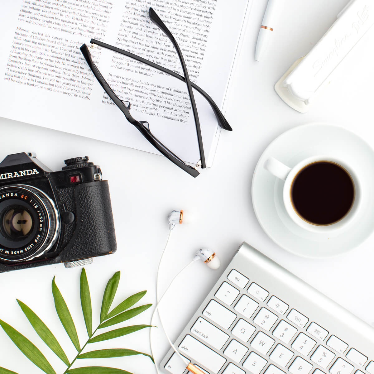Camera with white coffee cup on a desk with glasses and keyboard