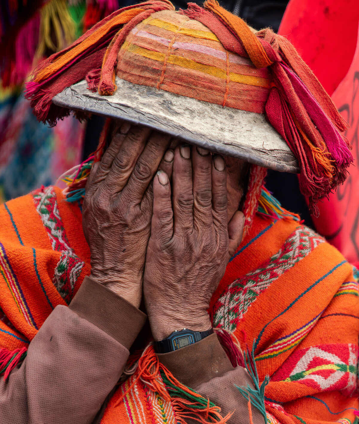 A Peruvian man wearing colourful, traditional dress holds his hands up to his face in despair