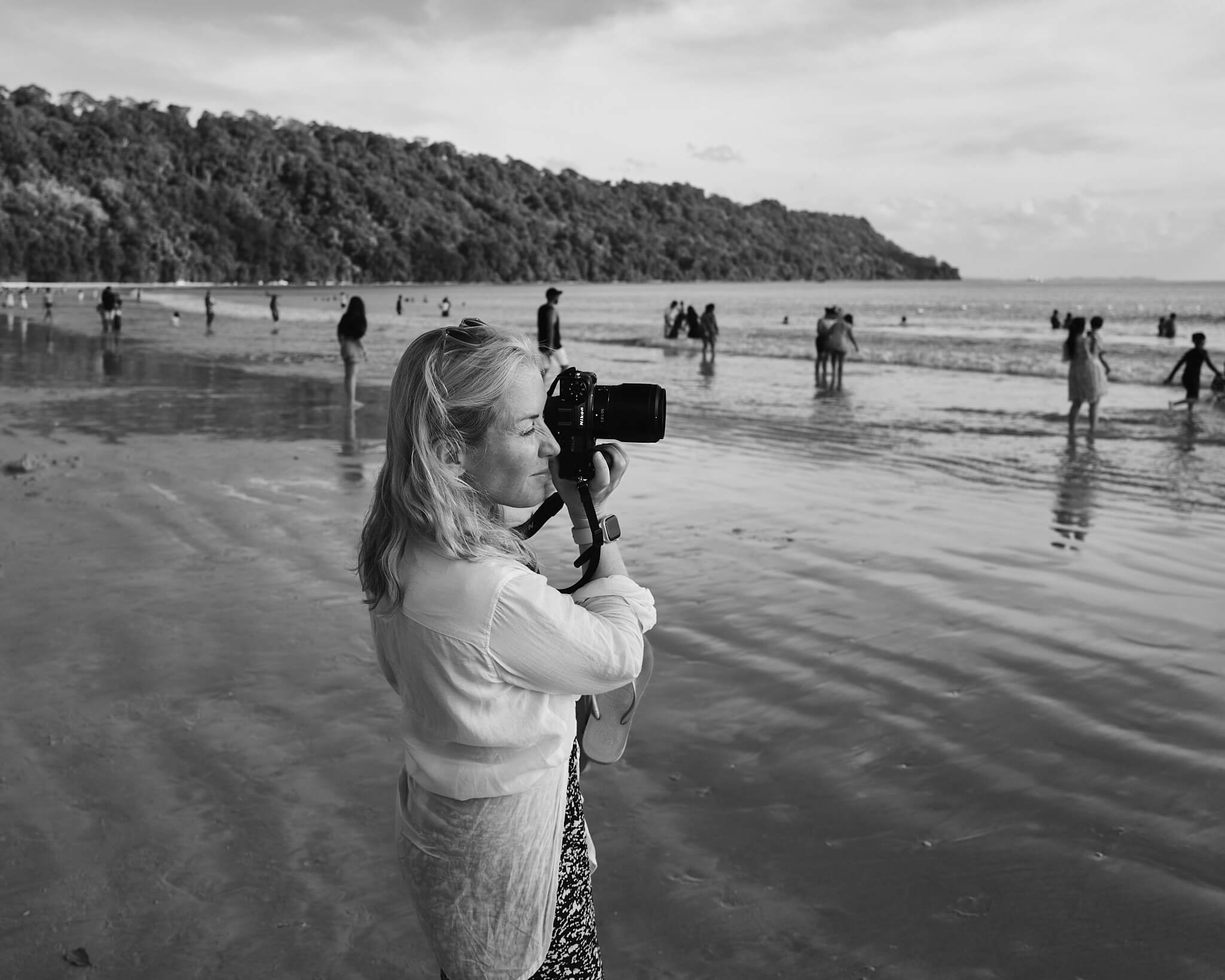 Portrait of photographer Hannah Maule-ffinch with a camera up to her face while on a beach