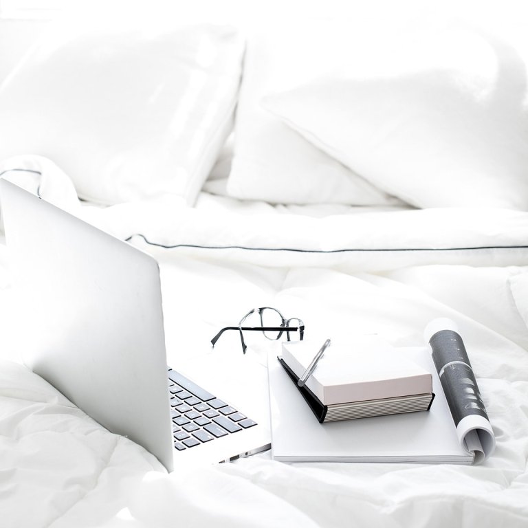 Laptop on bed with magazine notebook and glasses