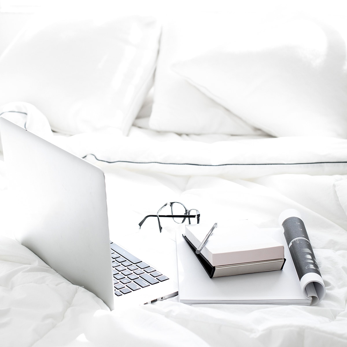 Laptop on bed with magazine notebook and glasses