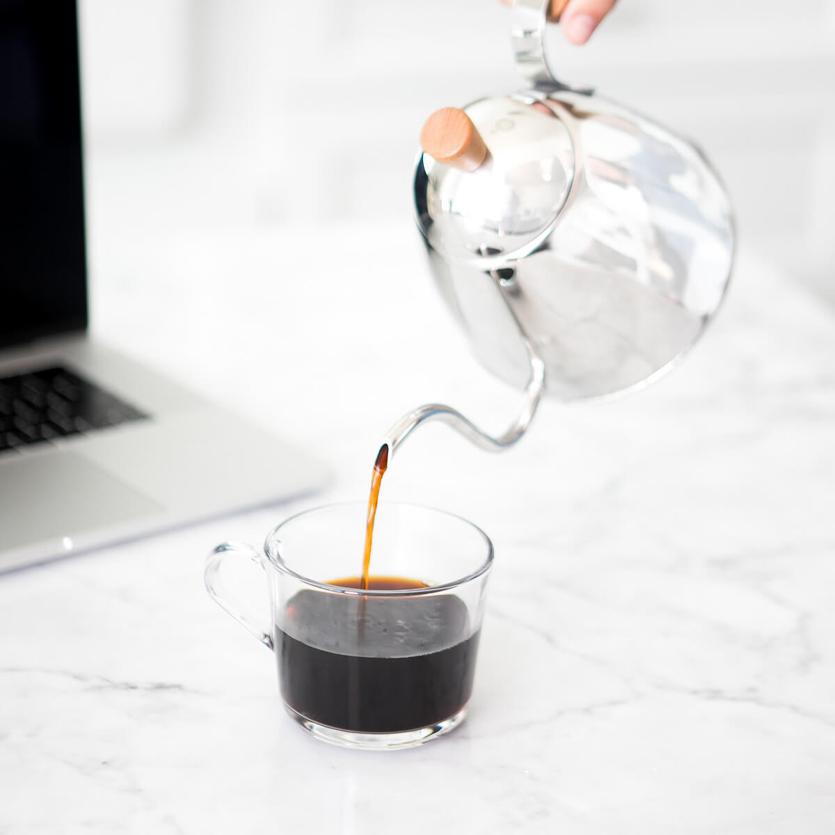 Silver teapot pouring tea into a clear mug