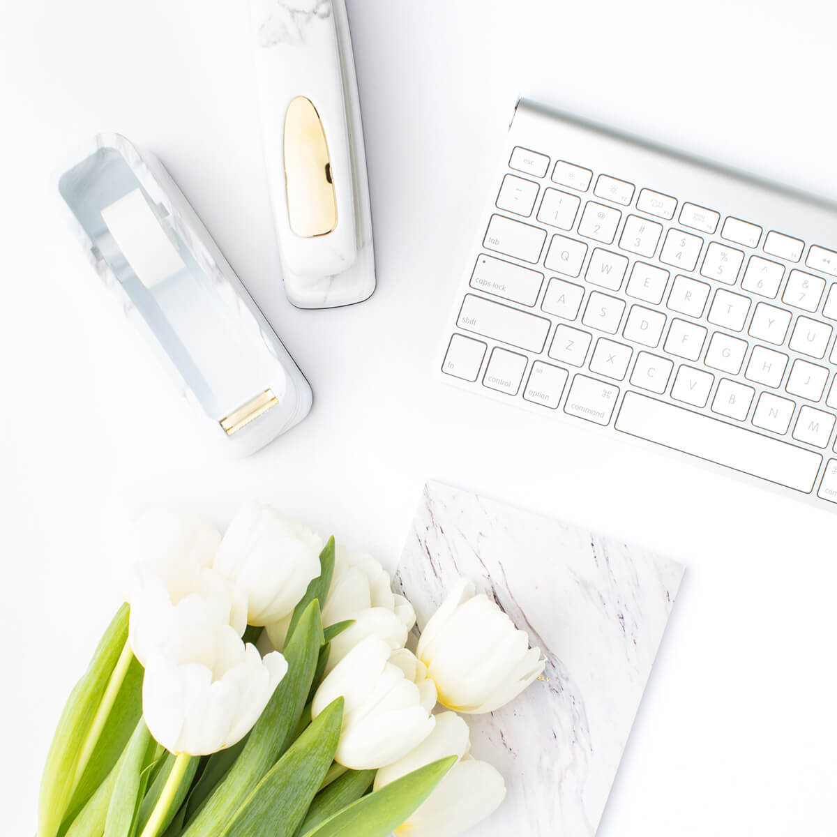 White tulips on a desk next to a keyboard and notebook