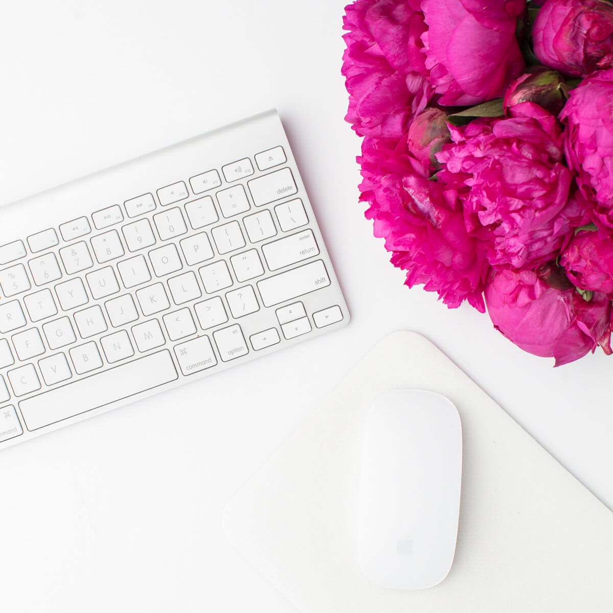 White desk and keyboard with computer mouse and pink flowers