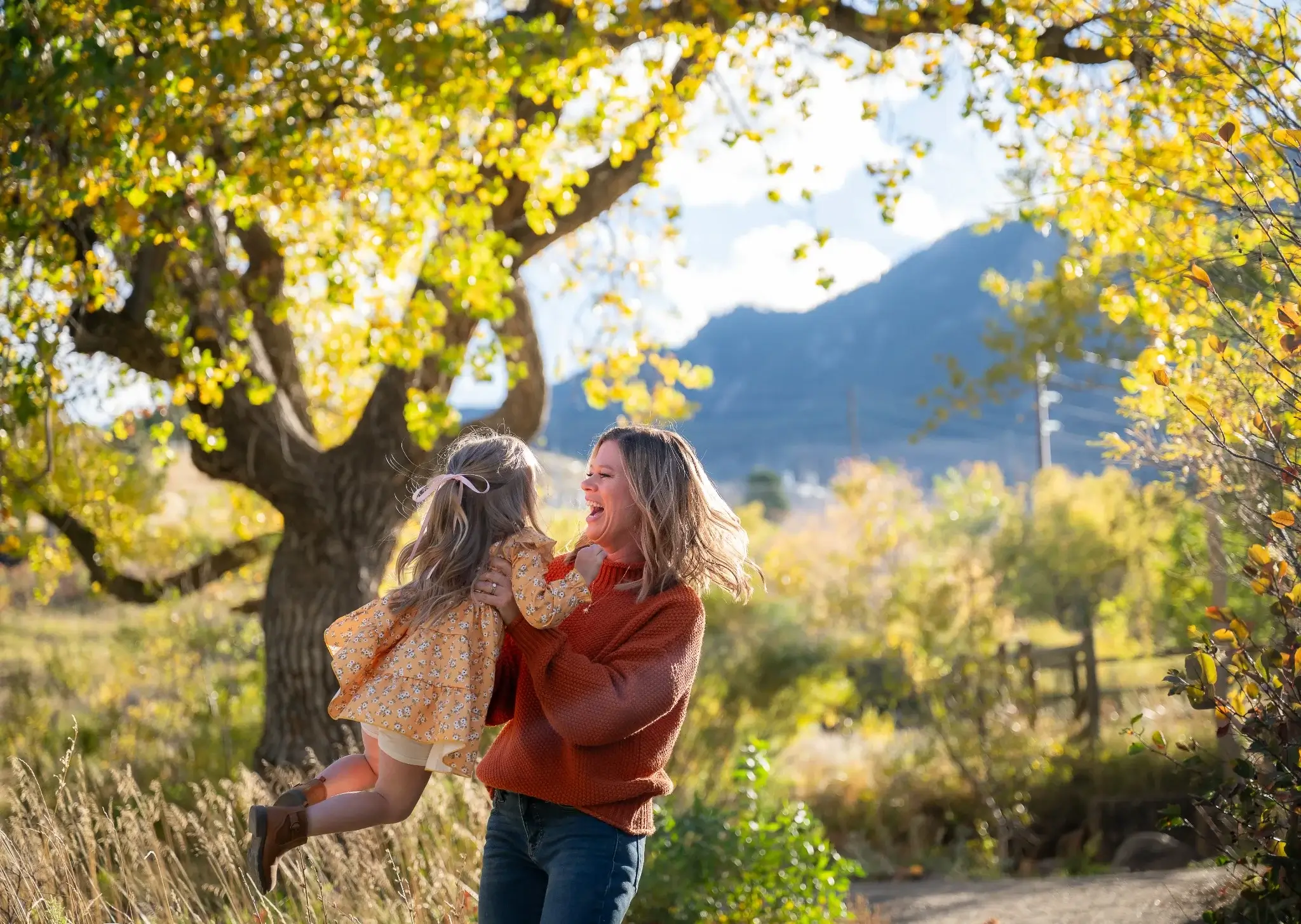 A smiling mum holding her daughter in the air during a bright autumn day