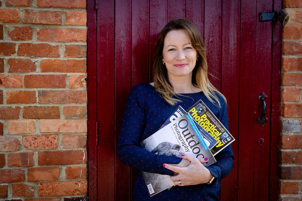 Zoe Hiljemark holding photography magazines against a red door and brick wall