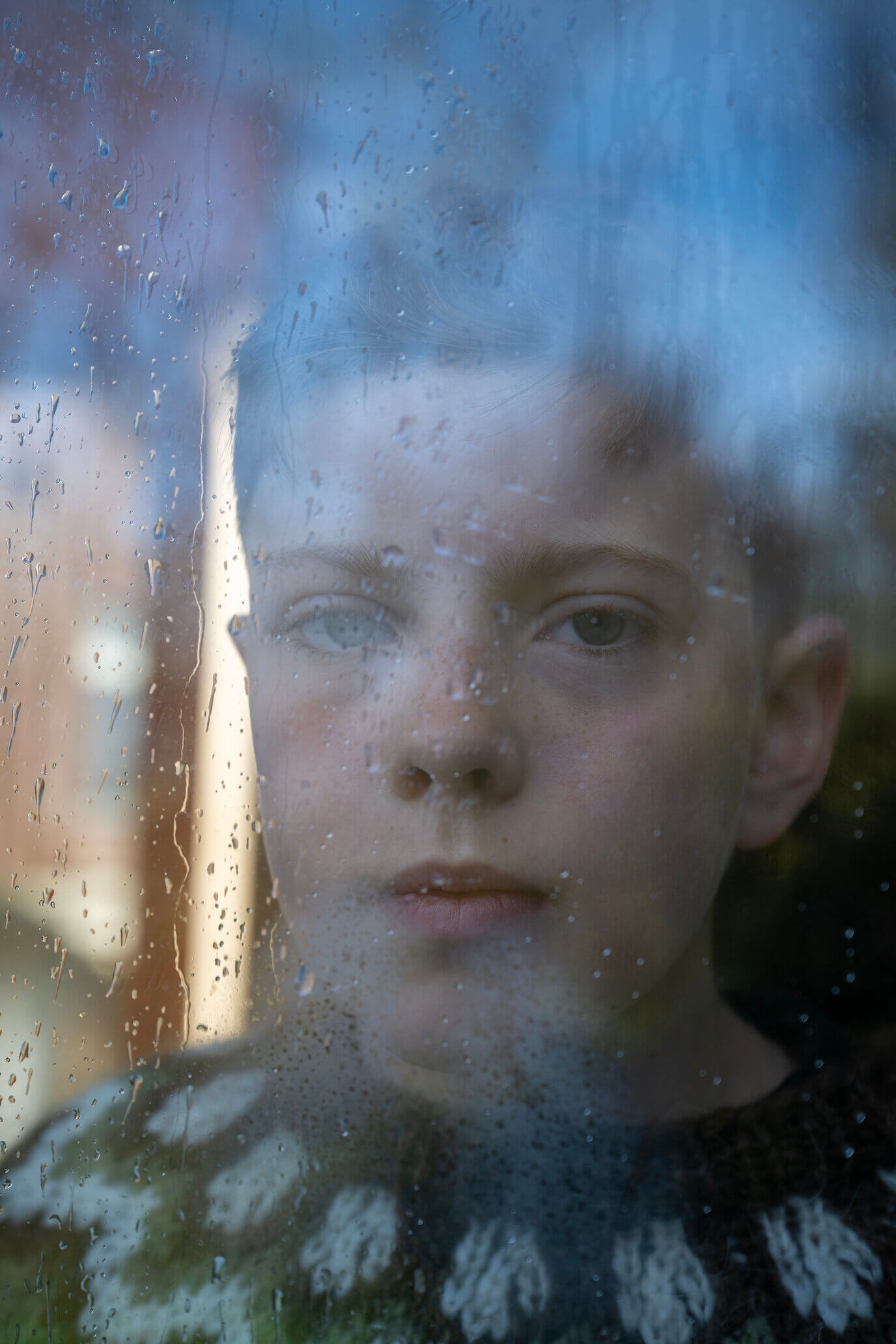 A young boy looking out the window with rain visible on the glass