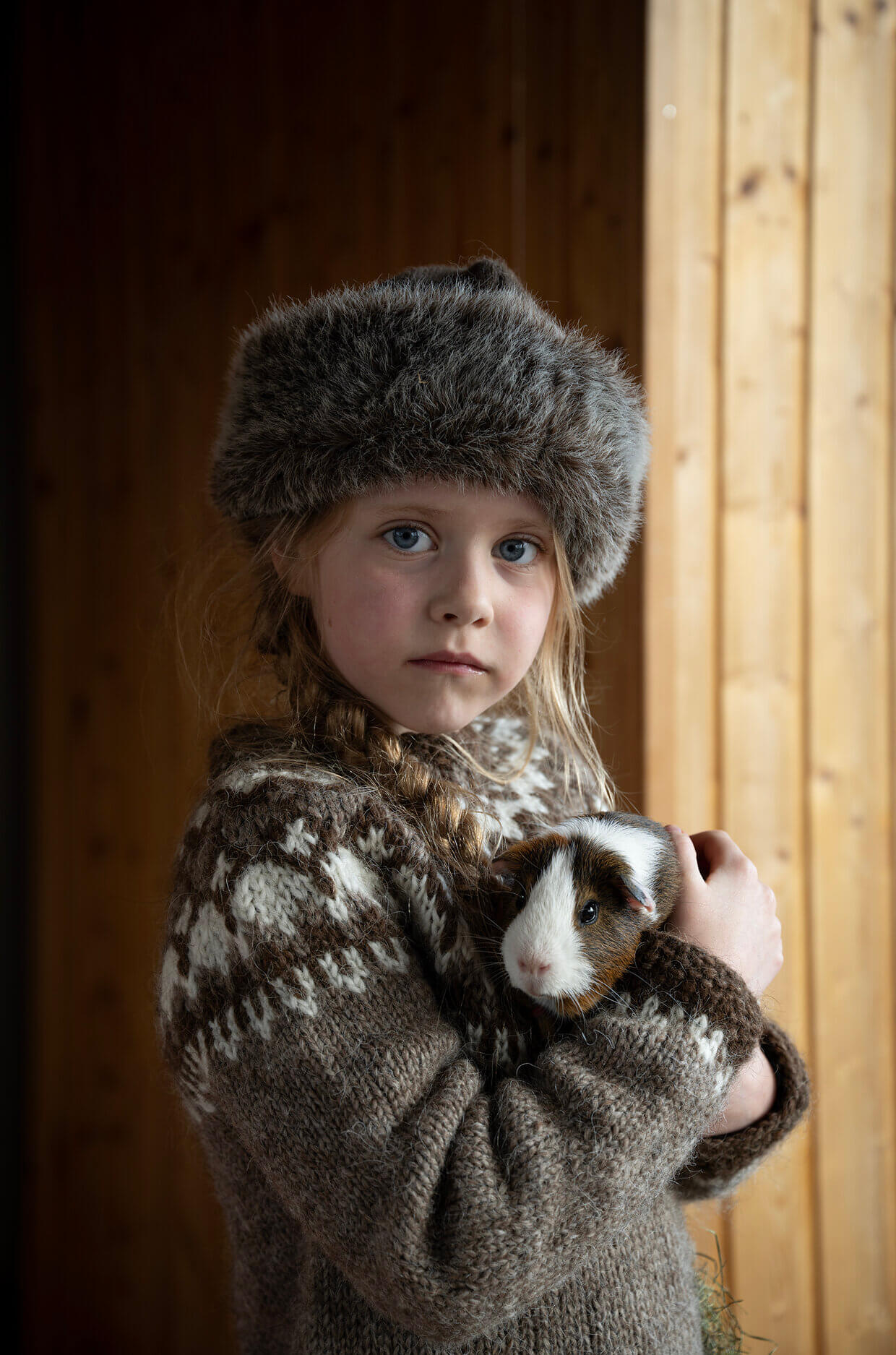 A young girl in a warm jumper and hat holding a guinea pig